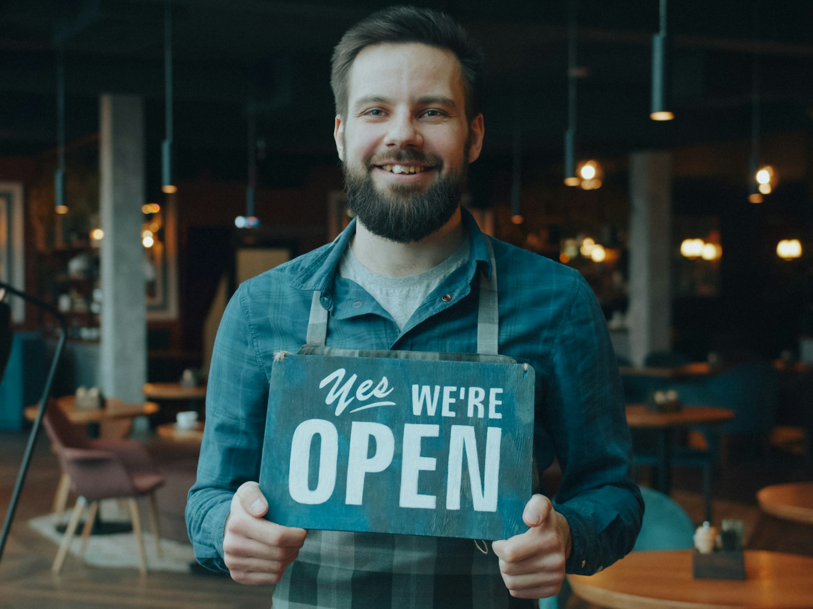Restaurant owner smiling and holding an Open sign