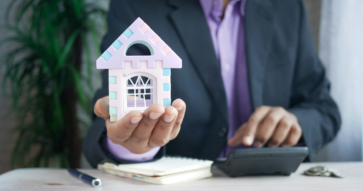 Business owner holding a small model house next to a calculator