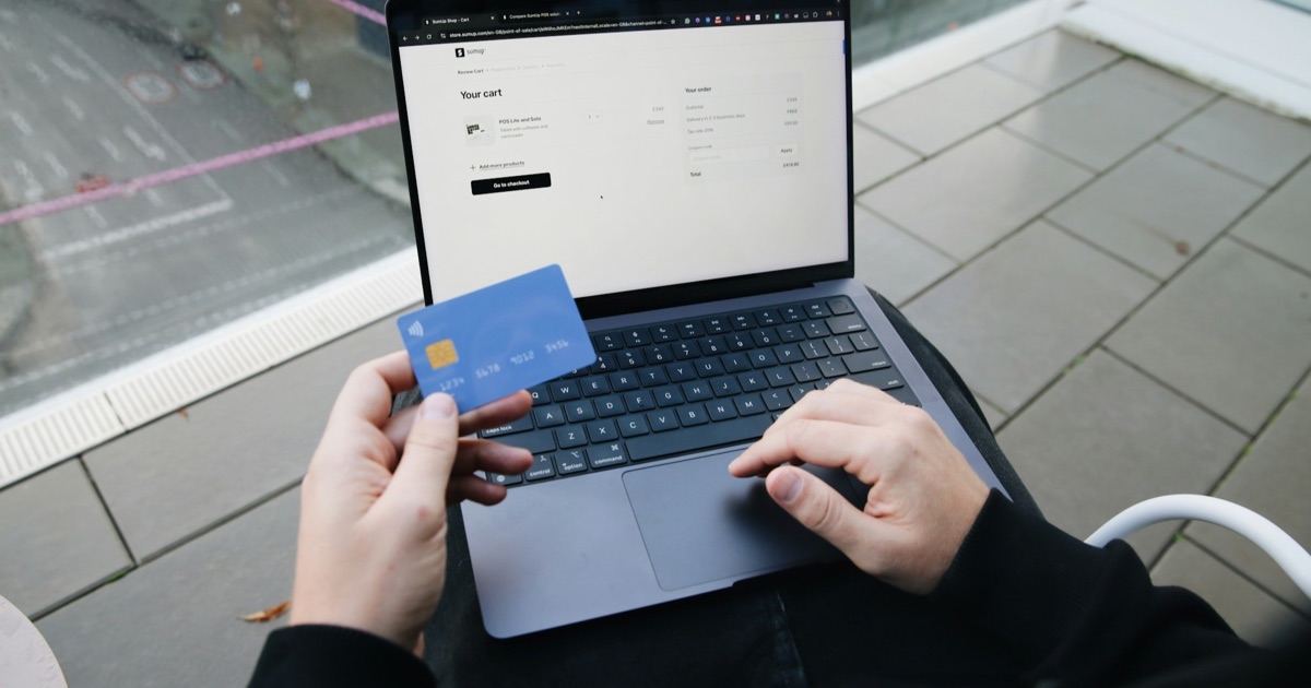 Person holding a credit card while completing a purchase on a laptop