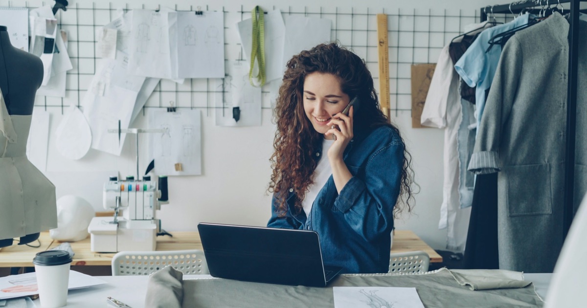 Small business owner on the phone while working on a laptop in her clothing studio